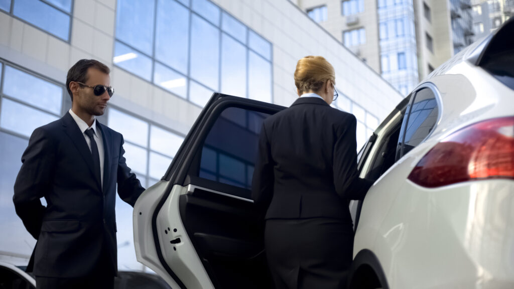 Personal driver waiting for boss on parking lot, helping her to get into car